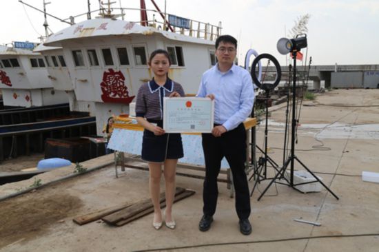 海鮮電商張夢琴與幫辦員手持食品經(jīng)營許可證合影。贛榆區(qū)委宣傳部供圖